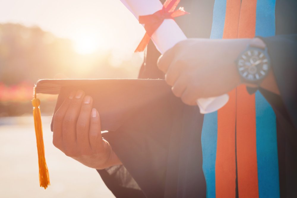 close-up-university-graduate-holding-degree-certificate-mortarboard